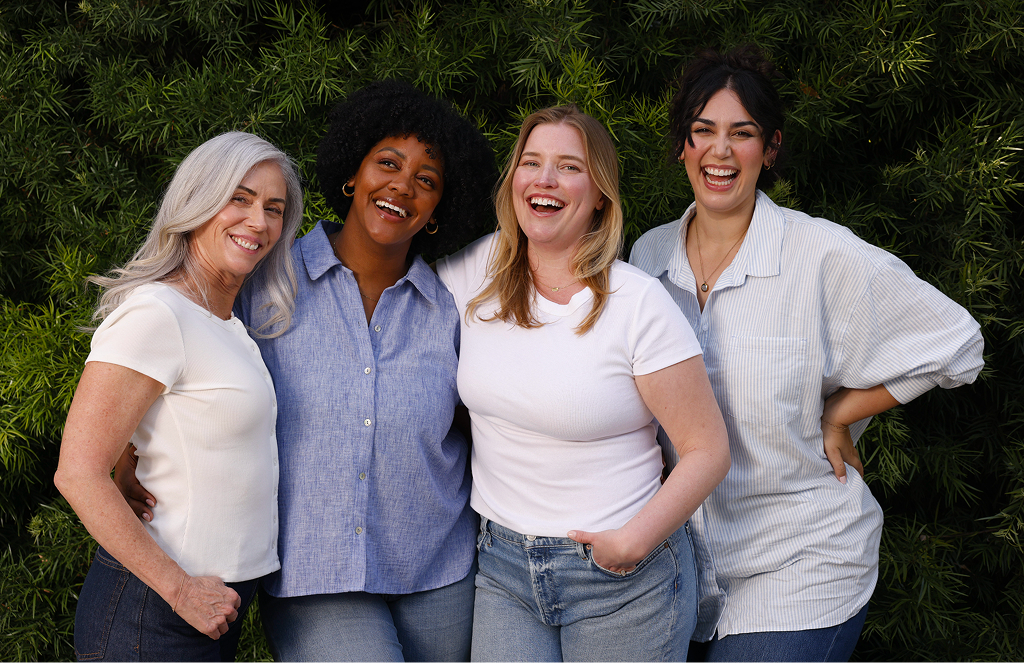 Four smiling women standing together outdoors in front of greenery