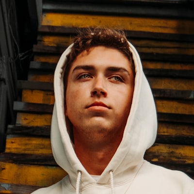 Young man wearing a white hoodie looking slightly upward in front of yellow and black stairs.