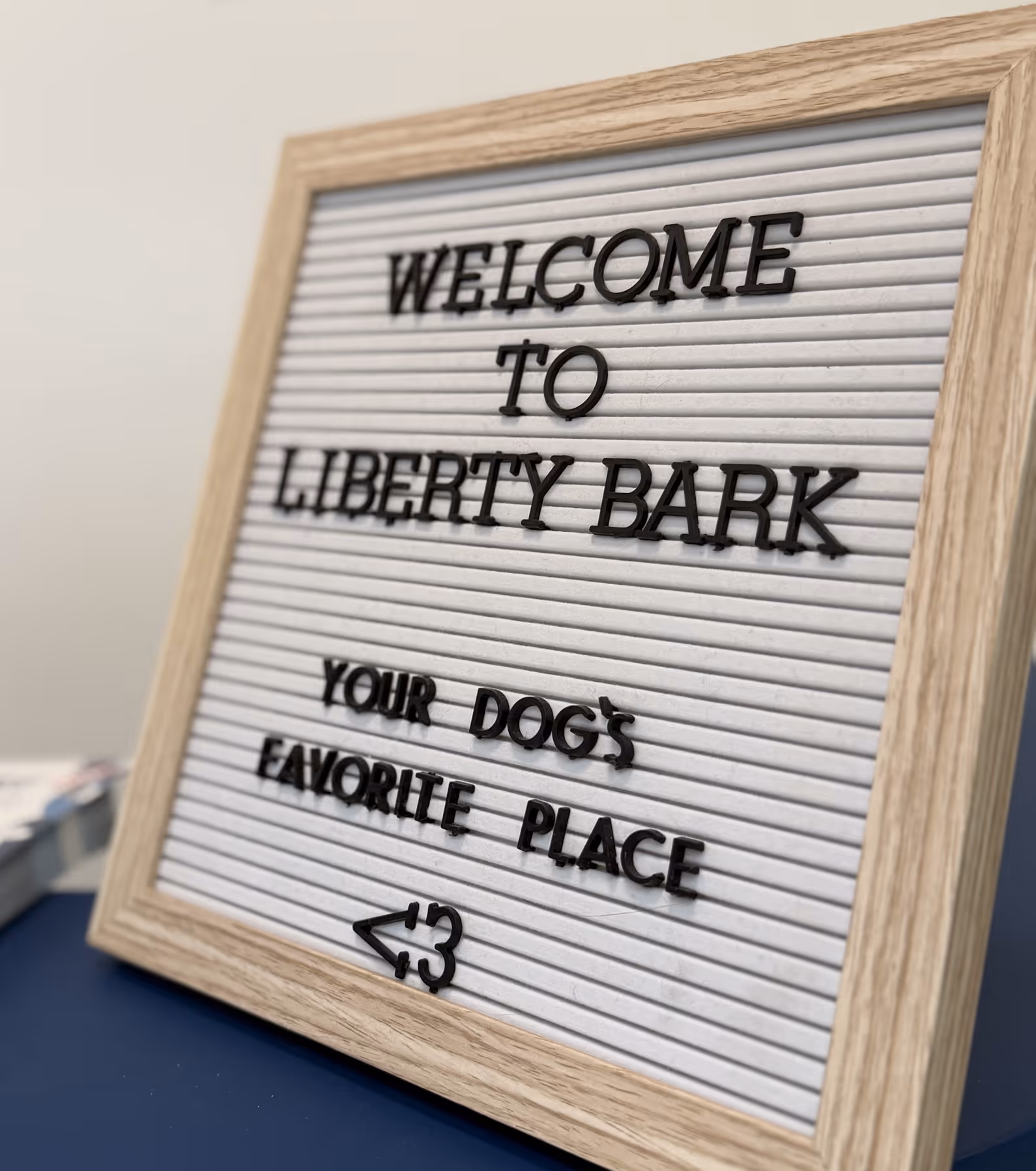 Letter board with wooden frame displaying the text 'WELCOME TO LIBERTY BARK YOUR DOG'S FAVORITE PLACE <3'.