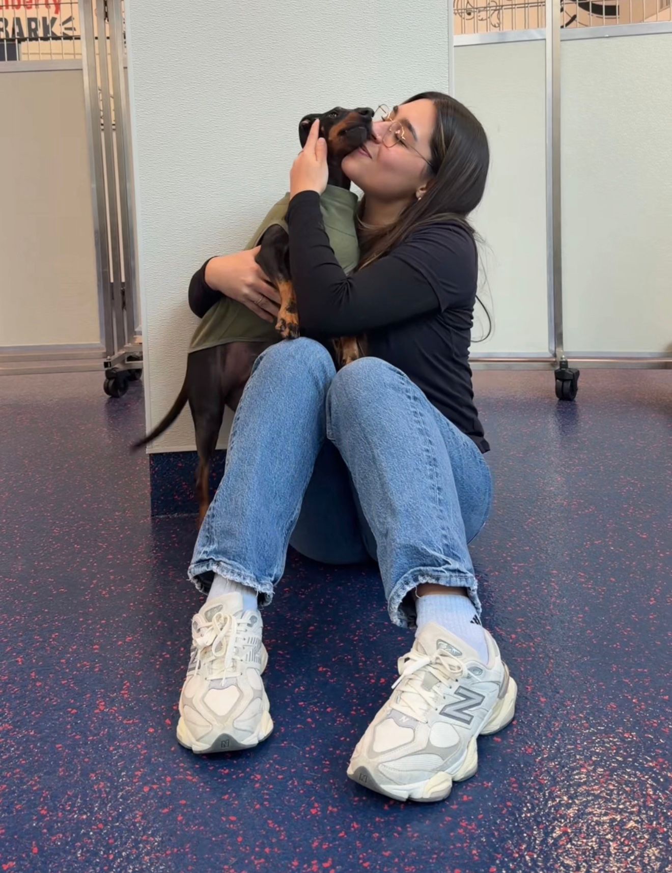 Woman holding and hugging a large curly brown dog indoors by a metal railing.