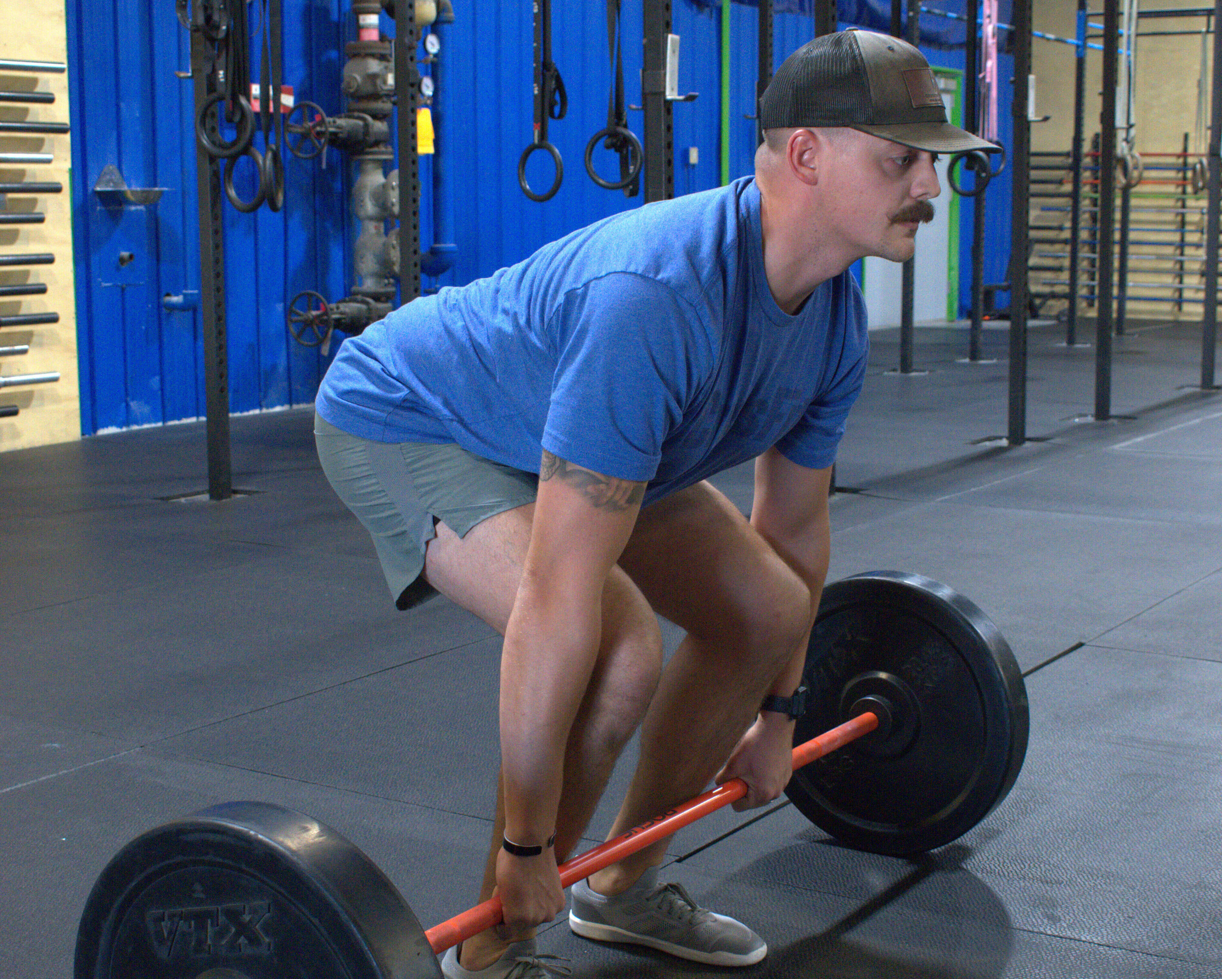 Man in a blue shirt and cap preparing to lift a barbell with black weights in a gym.