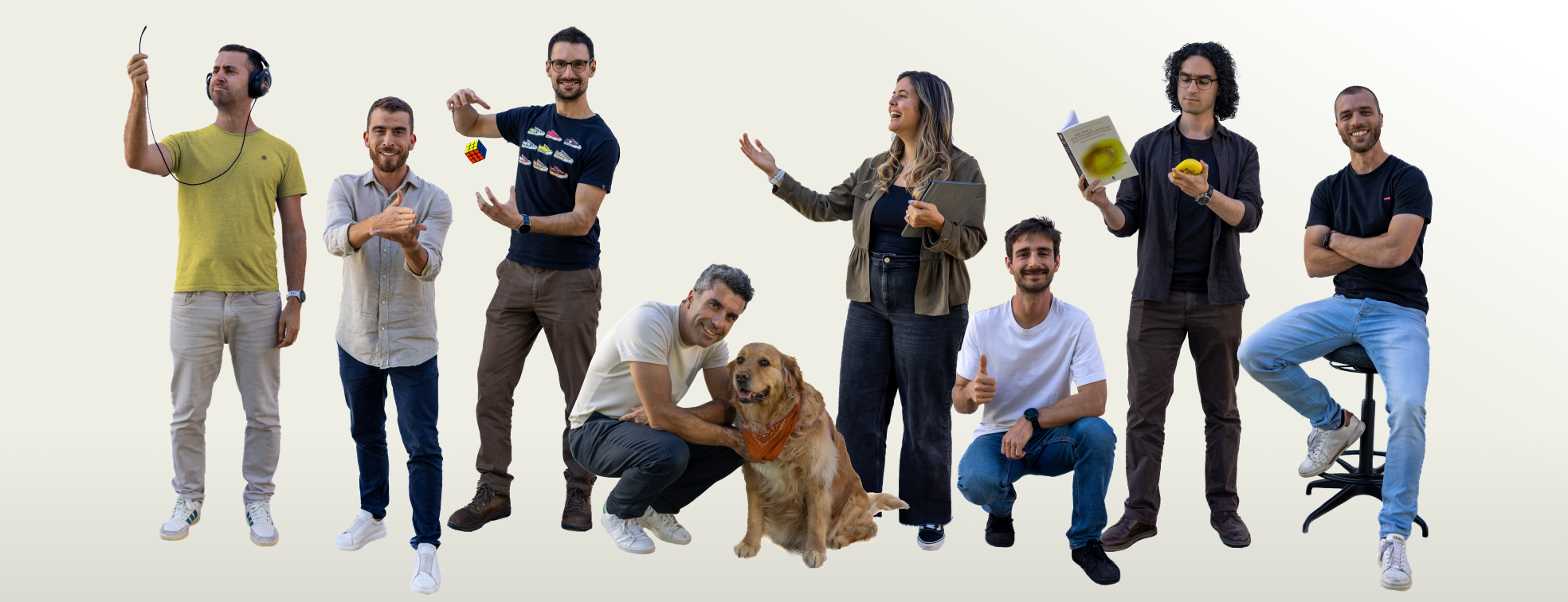 The team posing against a plain background, some sitting on stools and chairs, one holding a laptop, and another with a bag of chips.