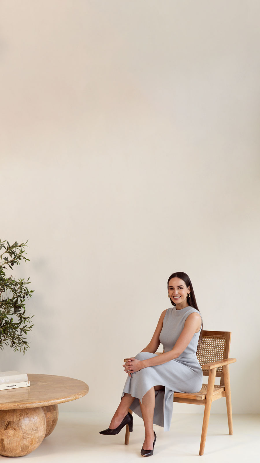 Shaina in a light coastal room, sitting near a coffee table.