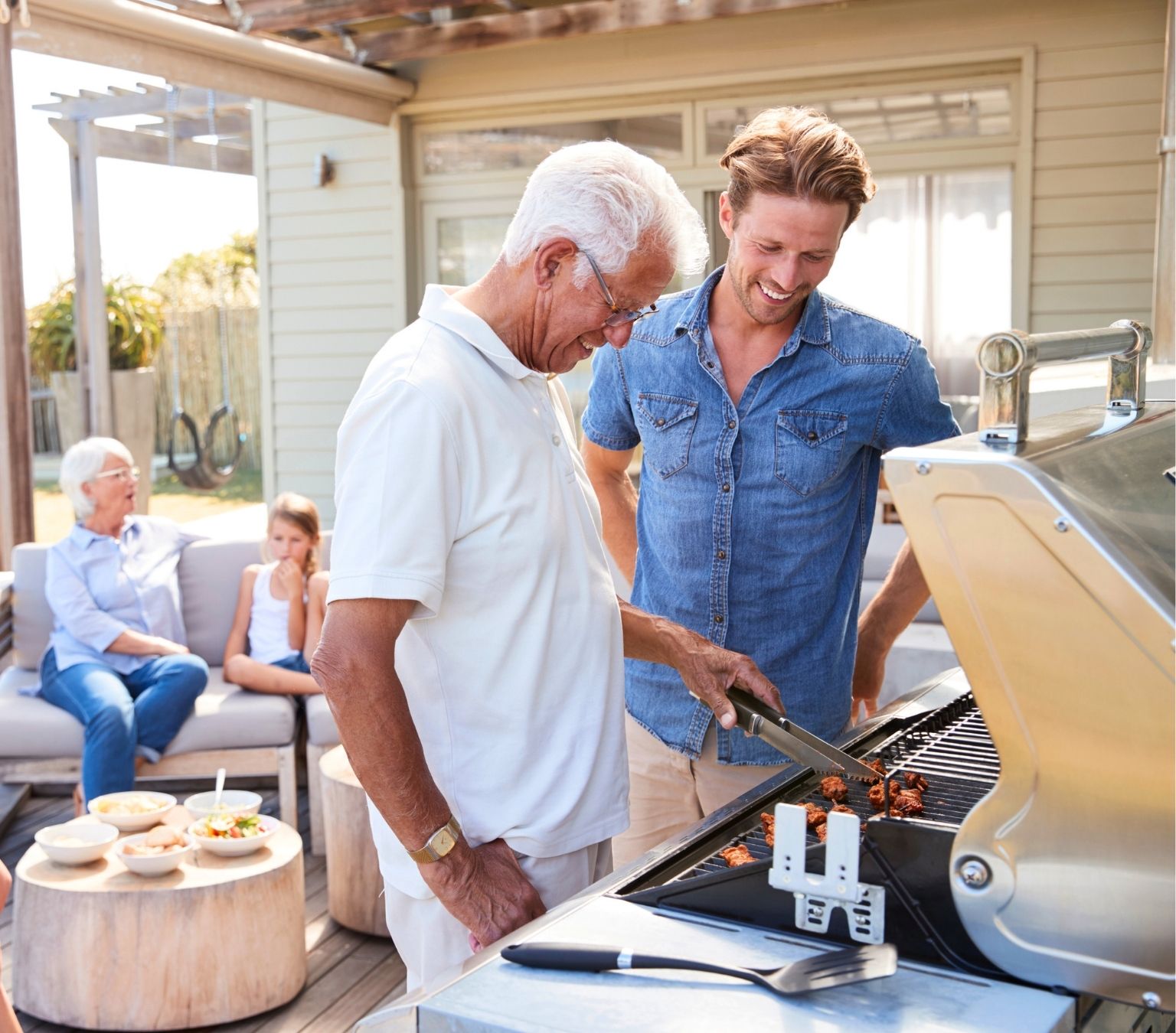 Friends in the backyard of a coastal home having a barbeque laughing and sharing food 