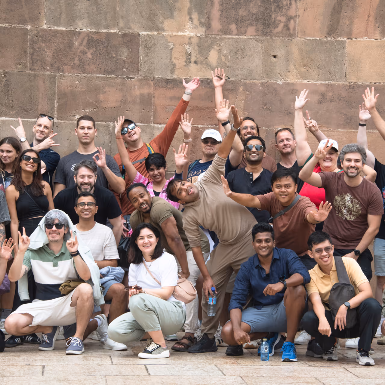The Flockler team smiling, posing with raised hands and playful gestures in front of a stone wall at a company event.
