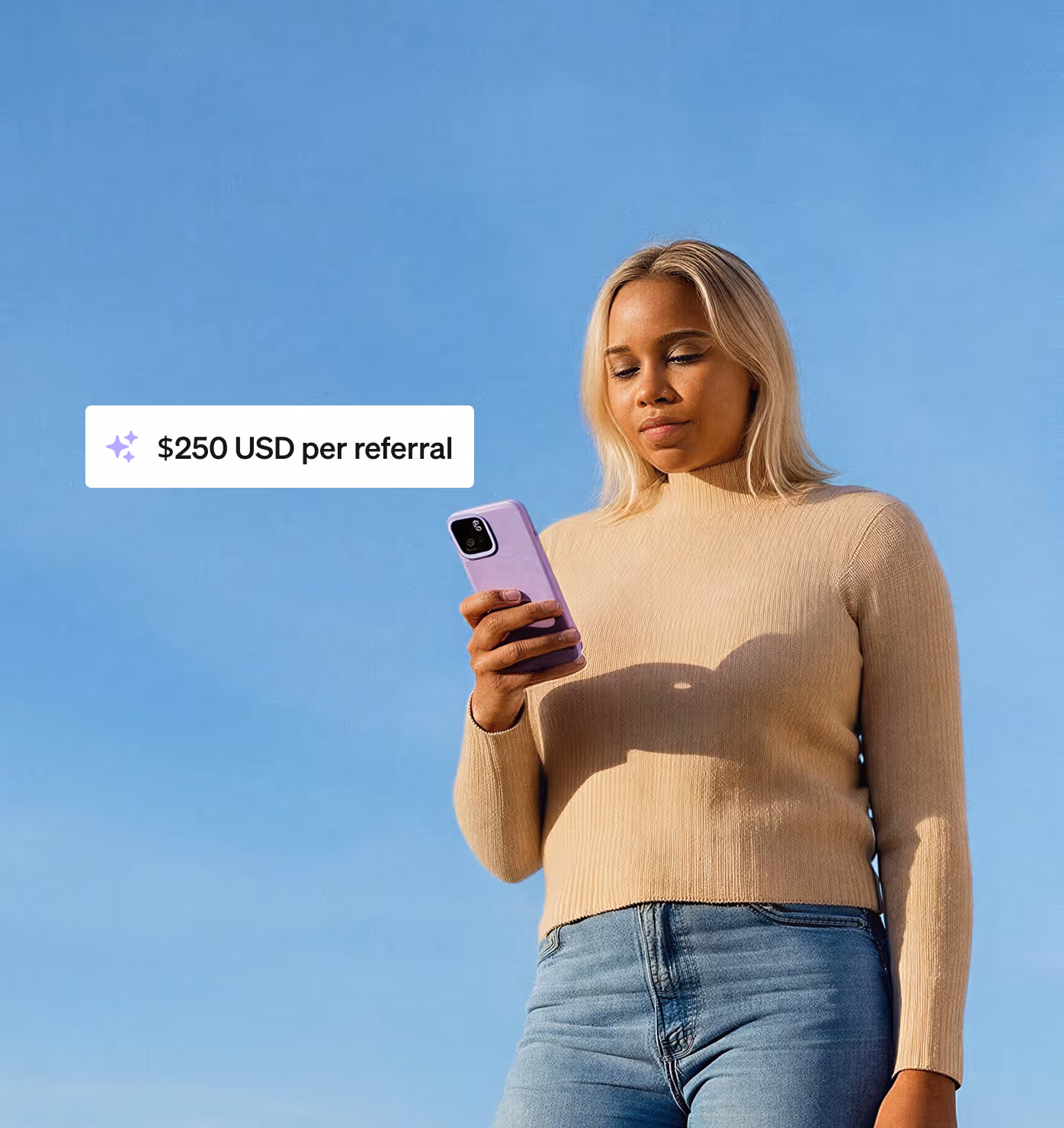 Woman in beige sweater and jeans looking at a phone with a $250 USD per referral text box against a clear blue sky.