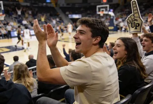 Excited young fans cheering and clapping in the stands during a basketball game.