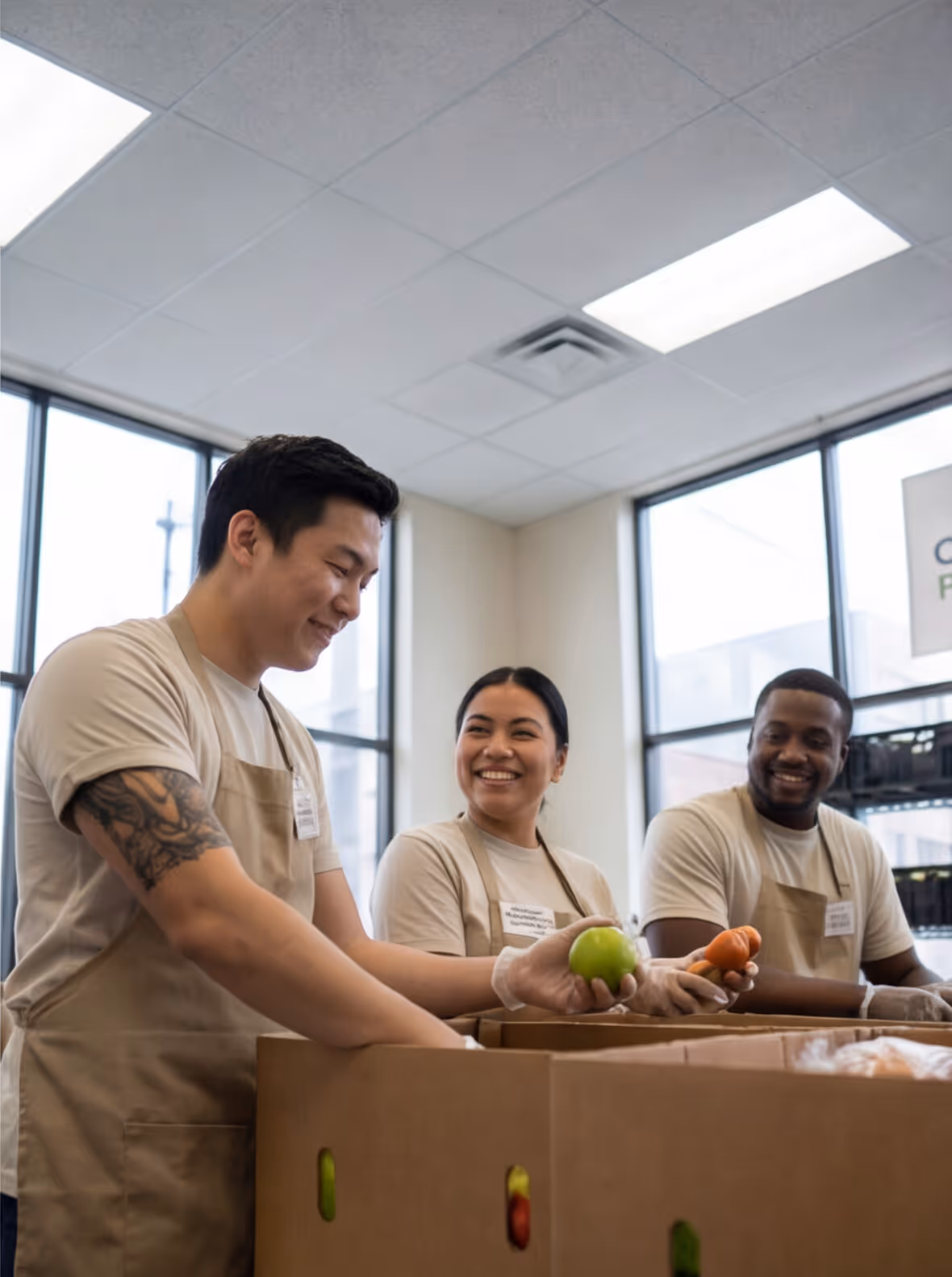 Three volunteers wearing aprons sorting fresh produce into boxes in a bright room.