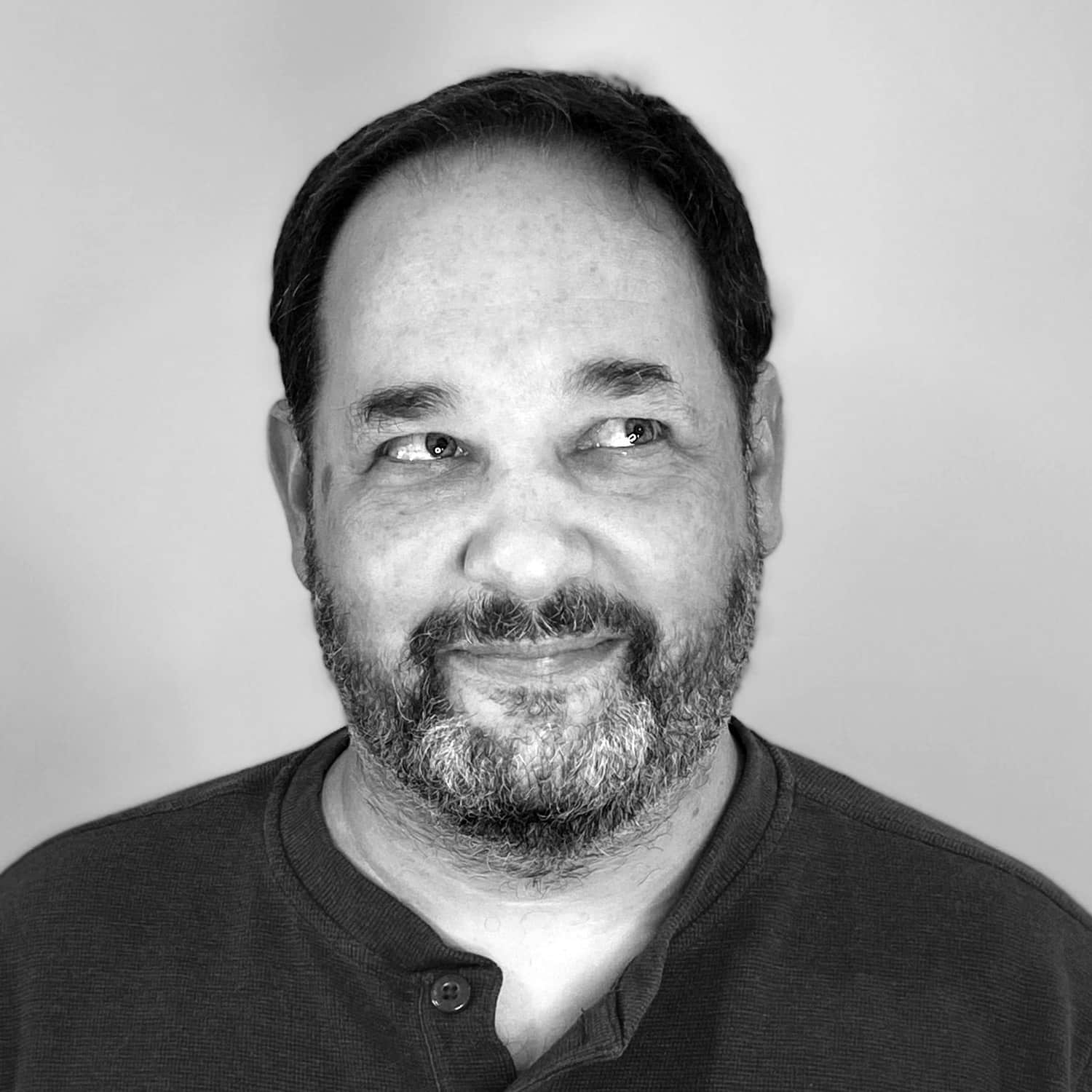 Man with beard looking to the side and smiling in a black and white portrait.