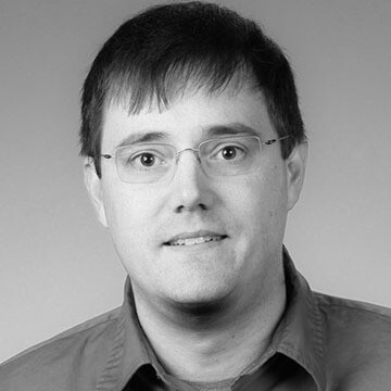 Black-and-white headshot of a man with glasses, short hair, and a collared shirt.
