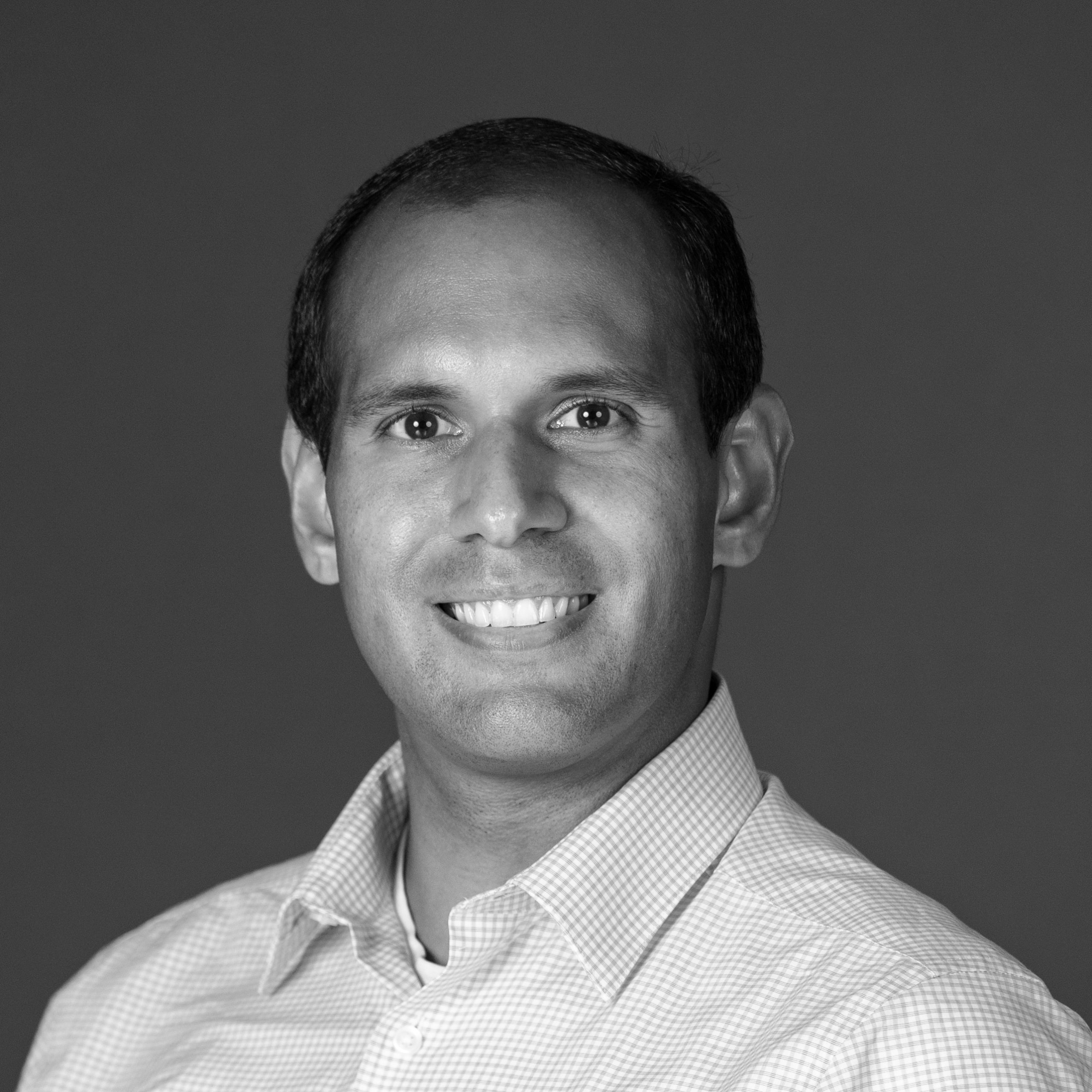 Smiling man in a checkered button-up shirt against a plain background, black and white photo.