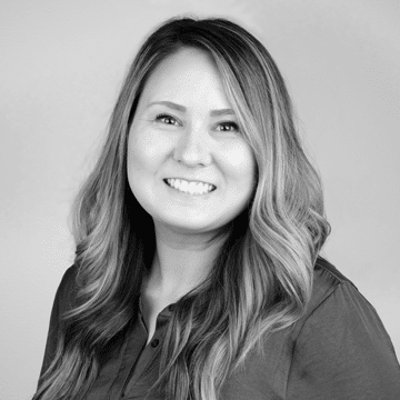 Smiling woman with long wavy hair wearing a button-up shirt on a gray background.