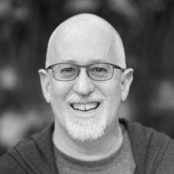Smiling bald man with glasses and white beard in a black and white portrait.