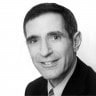Black and white portrait of a smiling middle-aged man in a suit and tie.