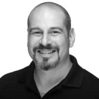Smiling bald man with goatee wearing a dark collared shirt against a white background.
