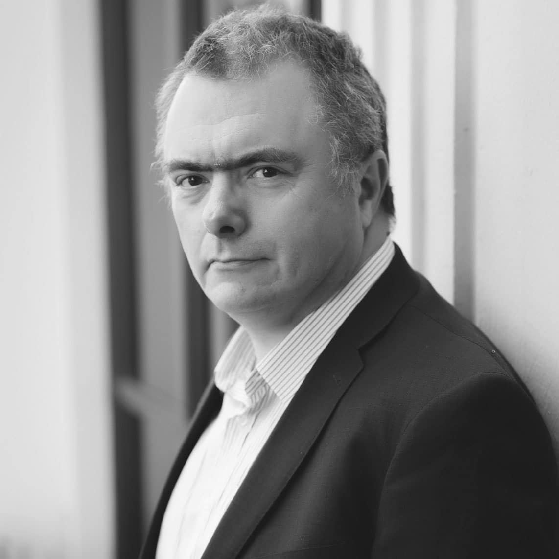 Black and white headshot of a man with short curly hair wearing a striped shirt and dark jacket.