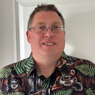 Man with glasses smiling, wearing a dark shirt with a green fern and raccoon print.