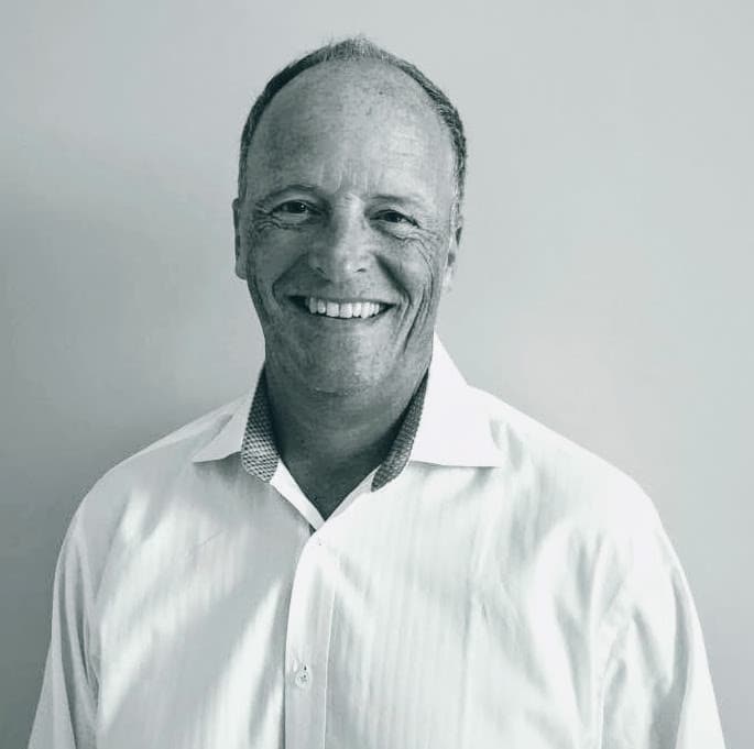 Smiling middle-aged man in a white collared shirt against a plain light background.
