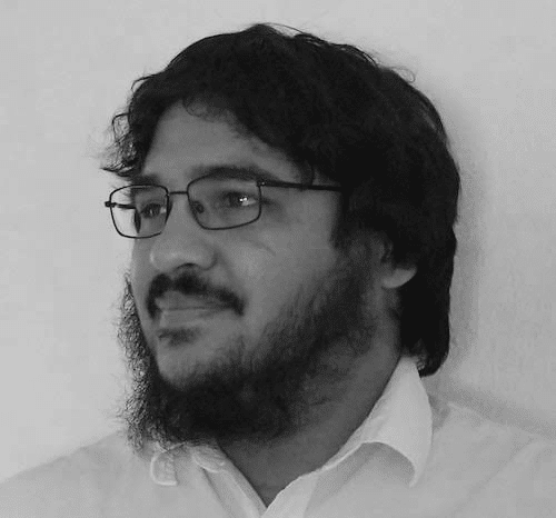 Bearded man with glasses and medium-length hair wearing a white collared shirt looking left.