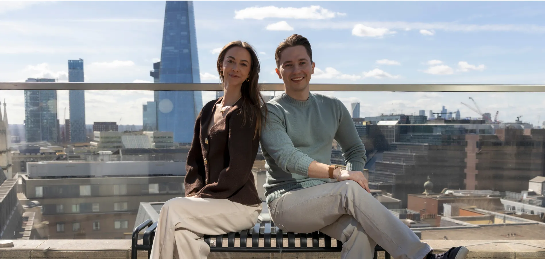 Bogdan Mihalache and Cynthia de Gelder sitting on a bench with a London background on a sunny day.