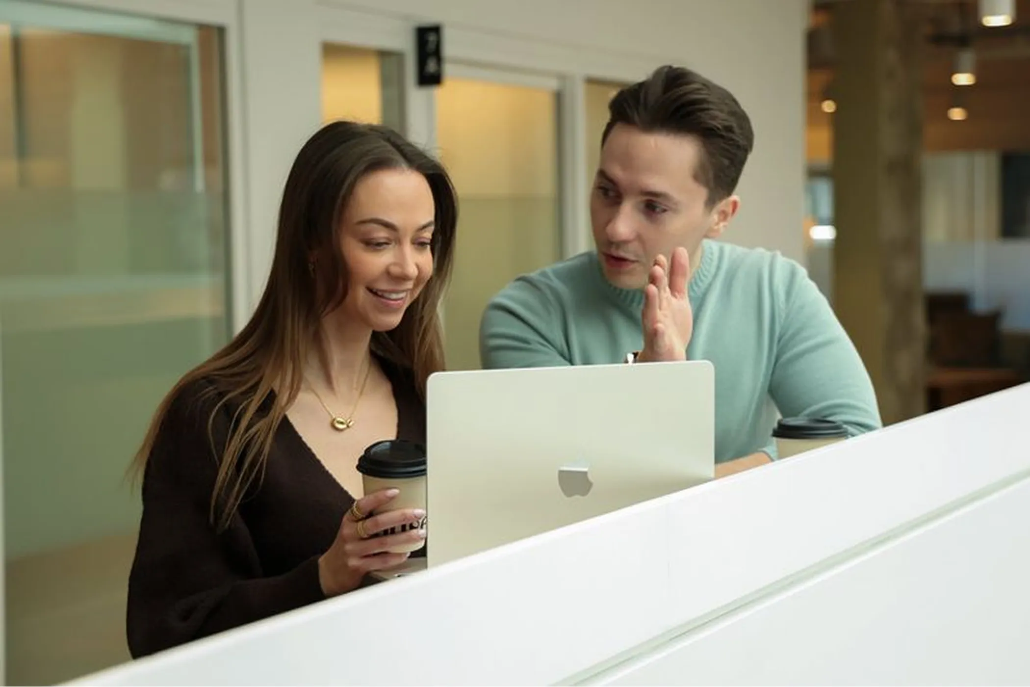 Cynthia de Gelder and Bogdan Mihalache in an office discussing and working on a laptop, with one holding a coffee cup.