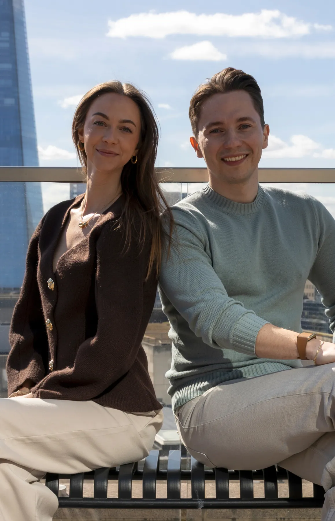 Bogdan and Cynthia sitting on a bench with a London background on a sunny day.
