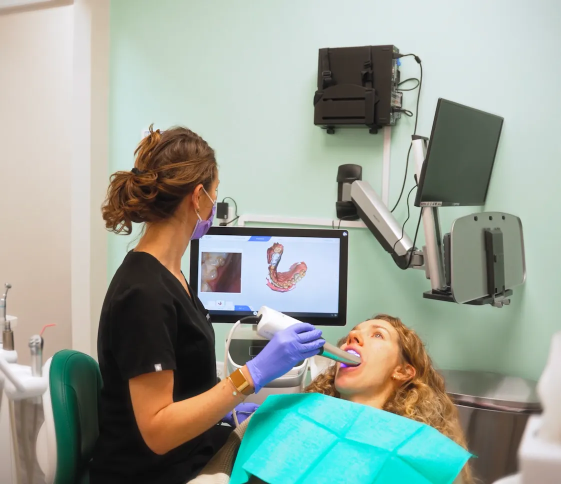 Dr. Anna Gazul using an intraoral scanner on a patient's open mouth with a digital dental image displayed on a screen.