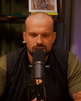 Man met kalend hoofd en baard spreekt in een microfoon tijdens een opname in een studio.