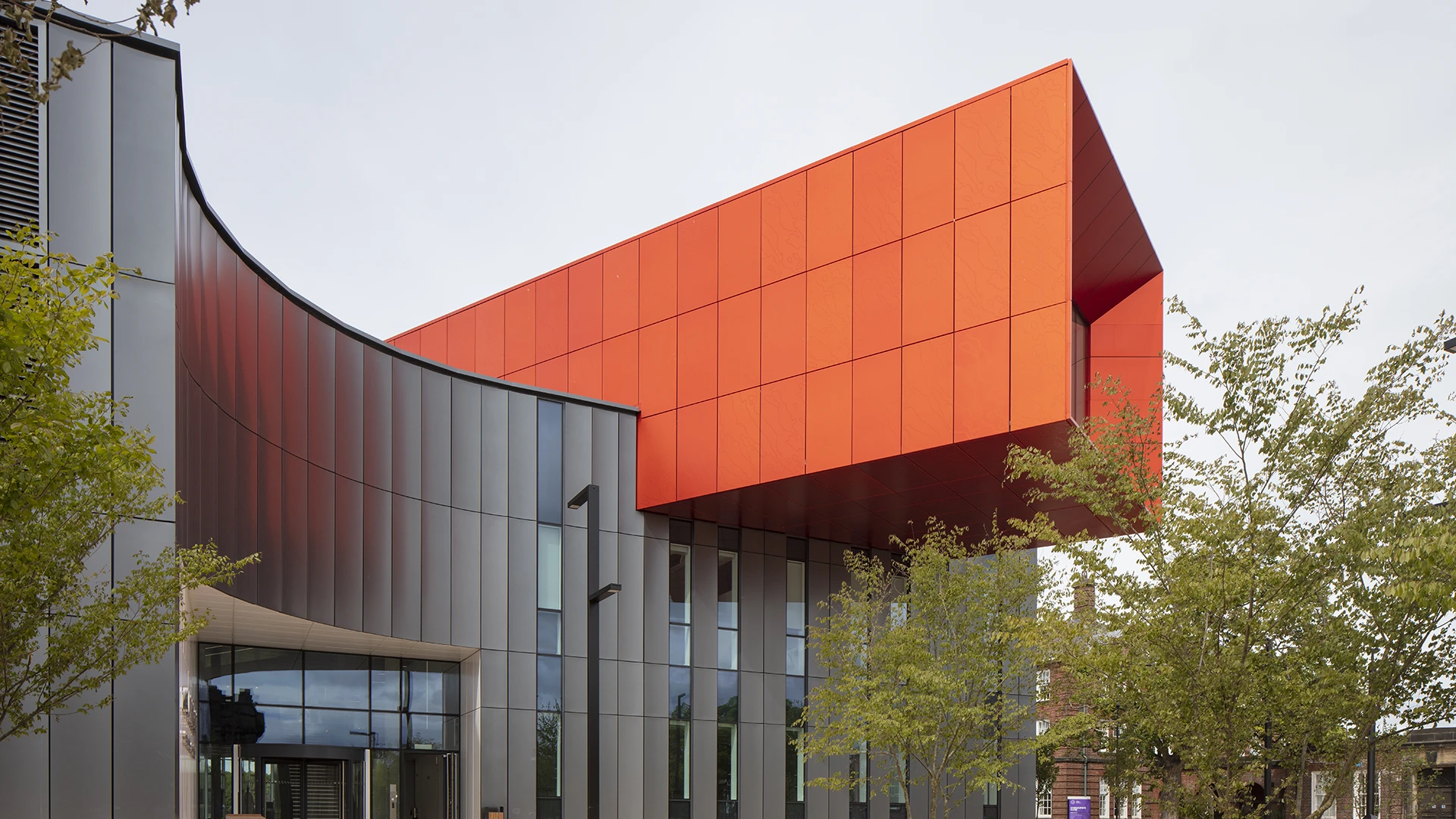 The red UnAtex anodised aluminium cantilever projecting from the curved grey anodised elevation of the Carnegie School of Sport