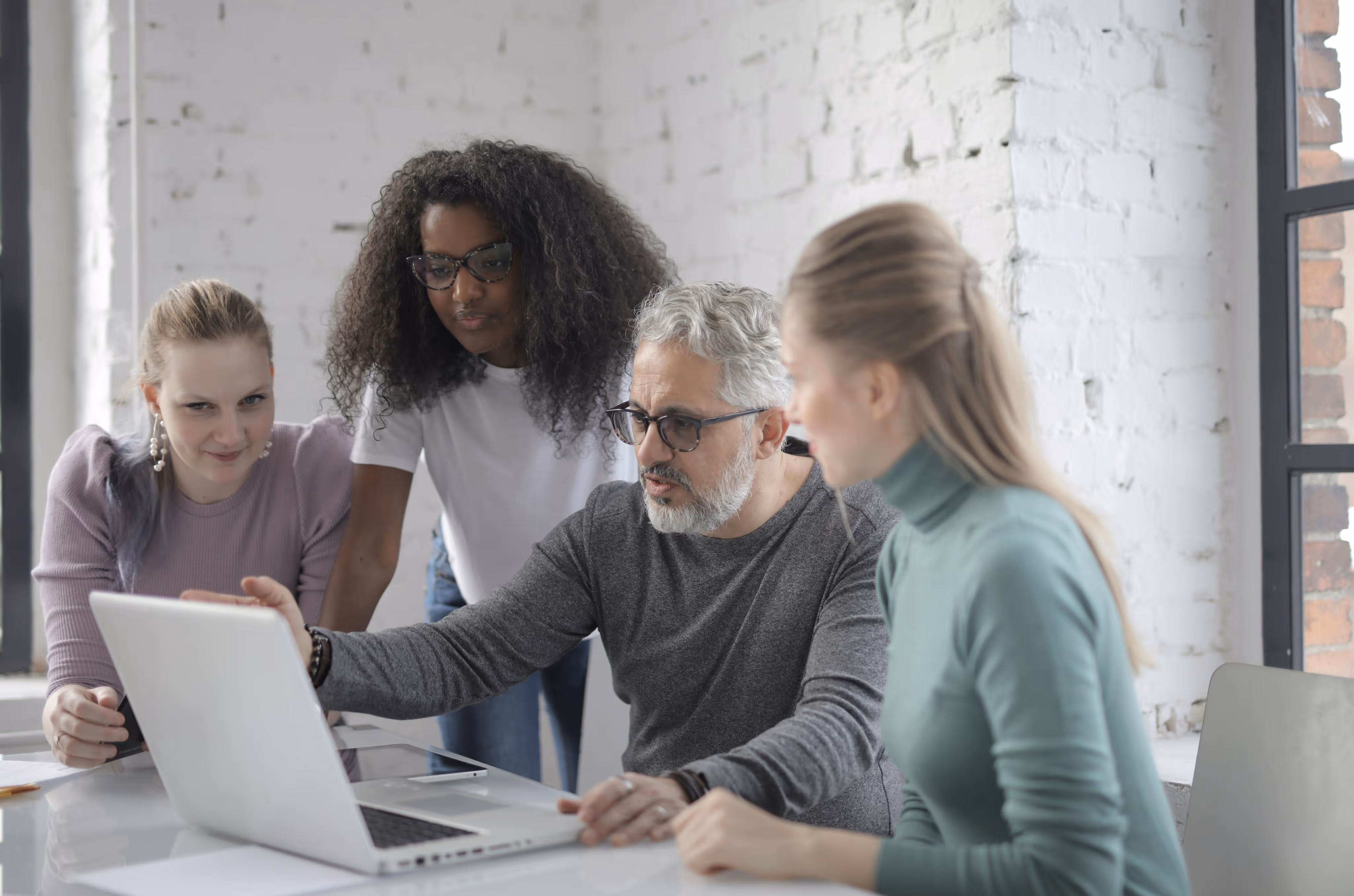 Four diverse colleagues collaborating and looking at a laptop screen in a bright modern office.