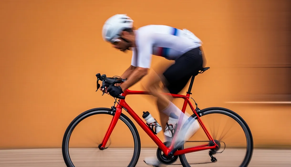 Cyclist in white and black gear riding a red road bike with motion blur against an orange background.