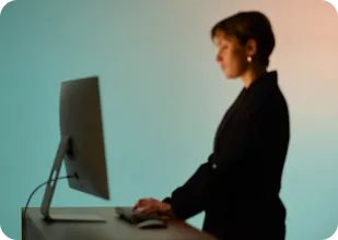 Woman in black using a desktop computer at a desk with a gradient blue and orange background.