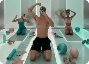 Three people posing in a modern gym studio with exercise mats, dumbbells, and fitness balls.