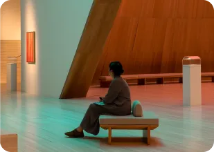Person sitting on a bench inside a modern art gallery with wooden architecture and minimalistic decor.