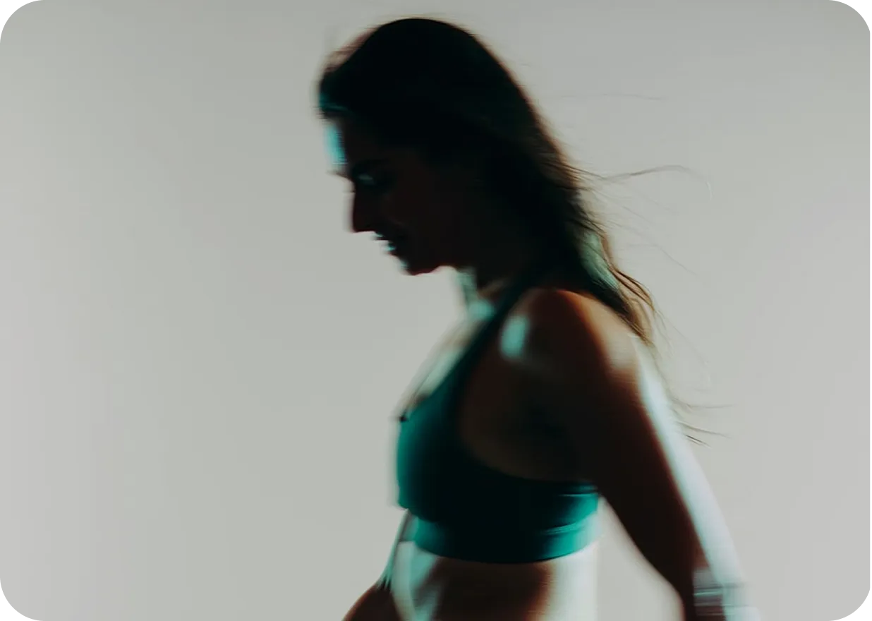 Side profile of a woman in a sports bra with flowing hair against a plain background.