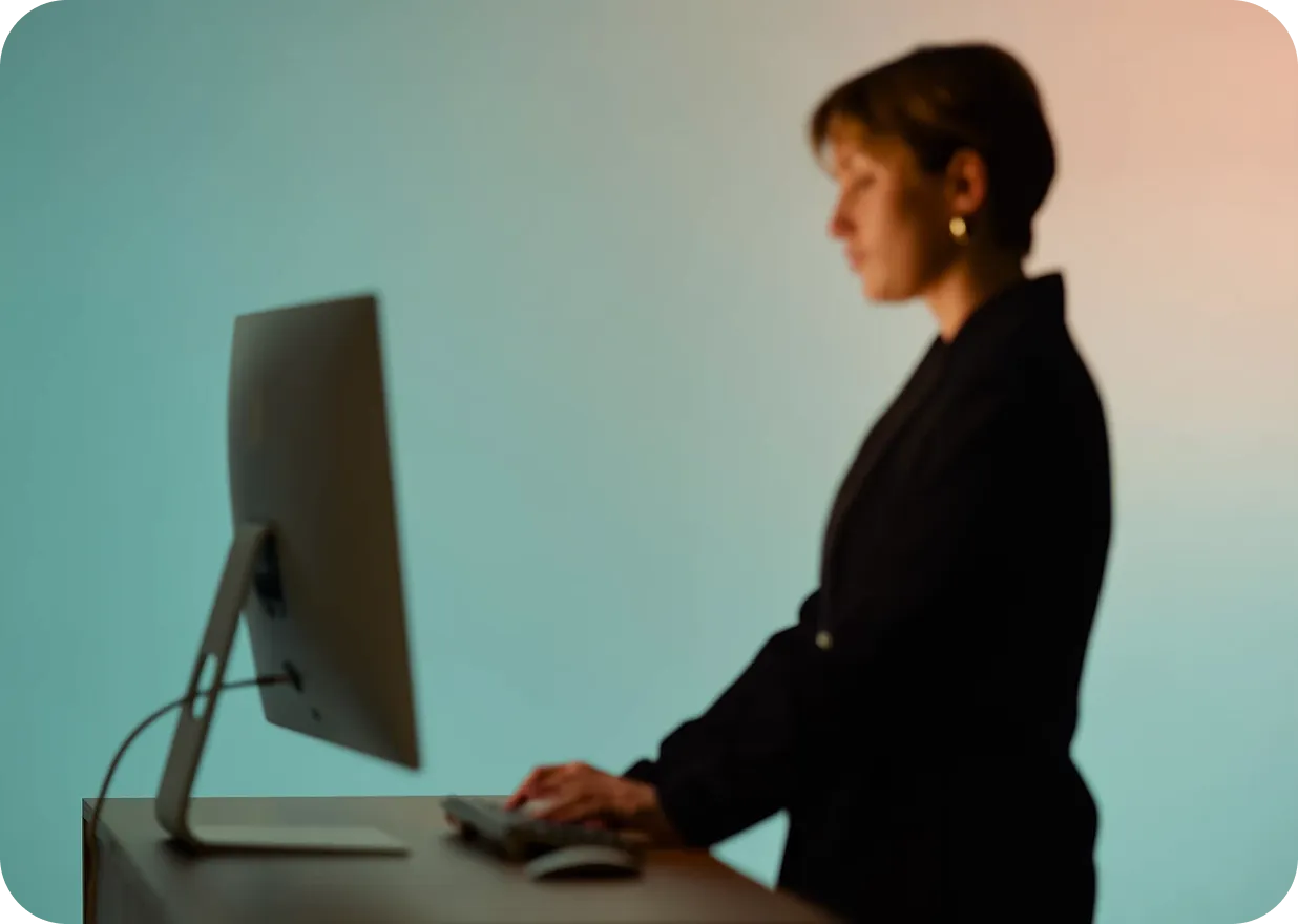 Side view of a person typing on a keyboard while standing at a desk with a computer monitor.