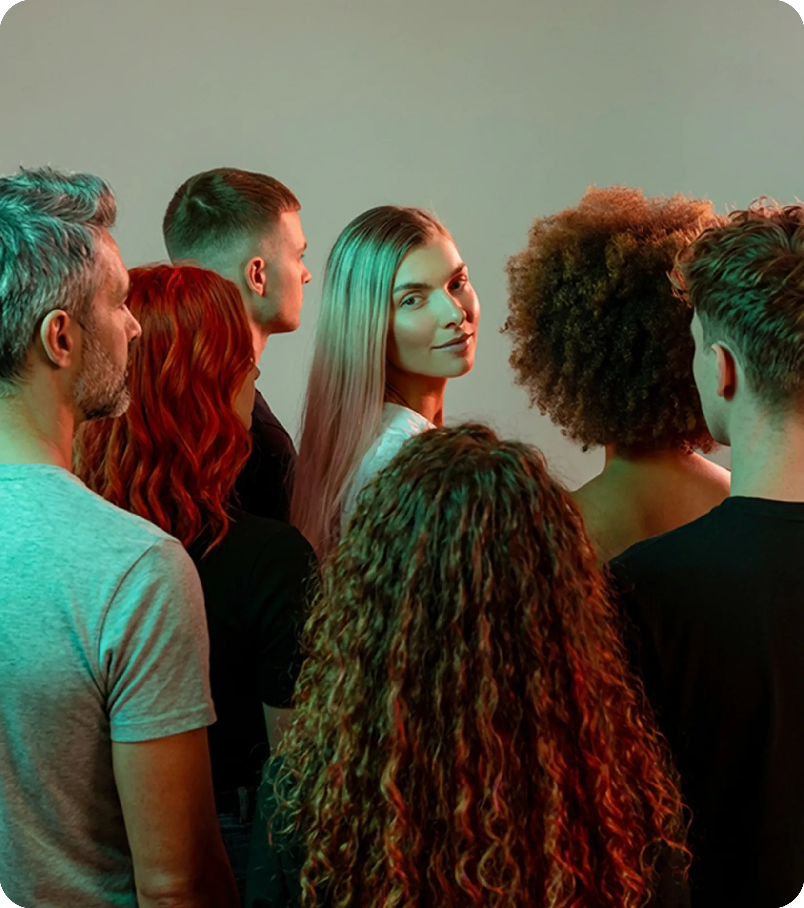 Group of seven diverse young adults standing close with one blonde woman facing the camera and others turned away.