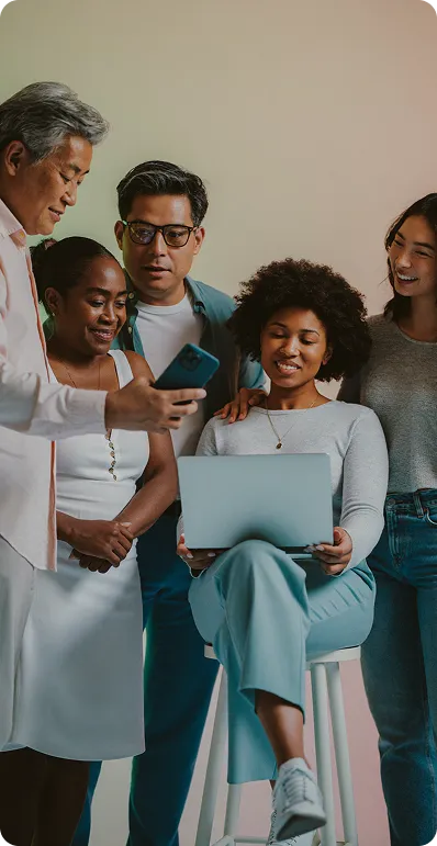 A diverse group of five people gathered, looking at a laptop and a smartphone, engaging collaboratively.