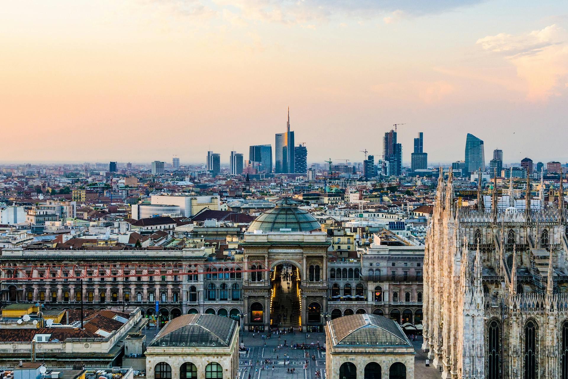 Skyline of Milan at sunset featuring the Milan Cathedral and the Galleria Vittorio Emanuele II with modern skyscrapers in the background.