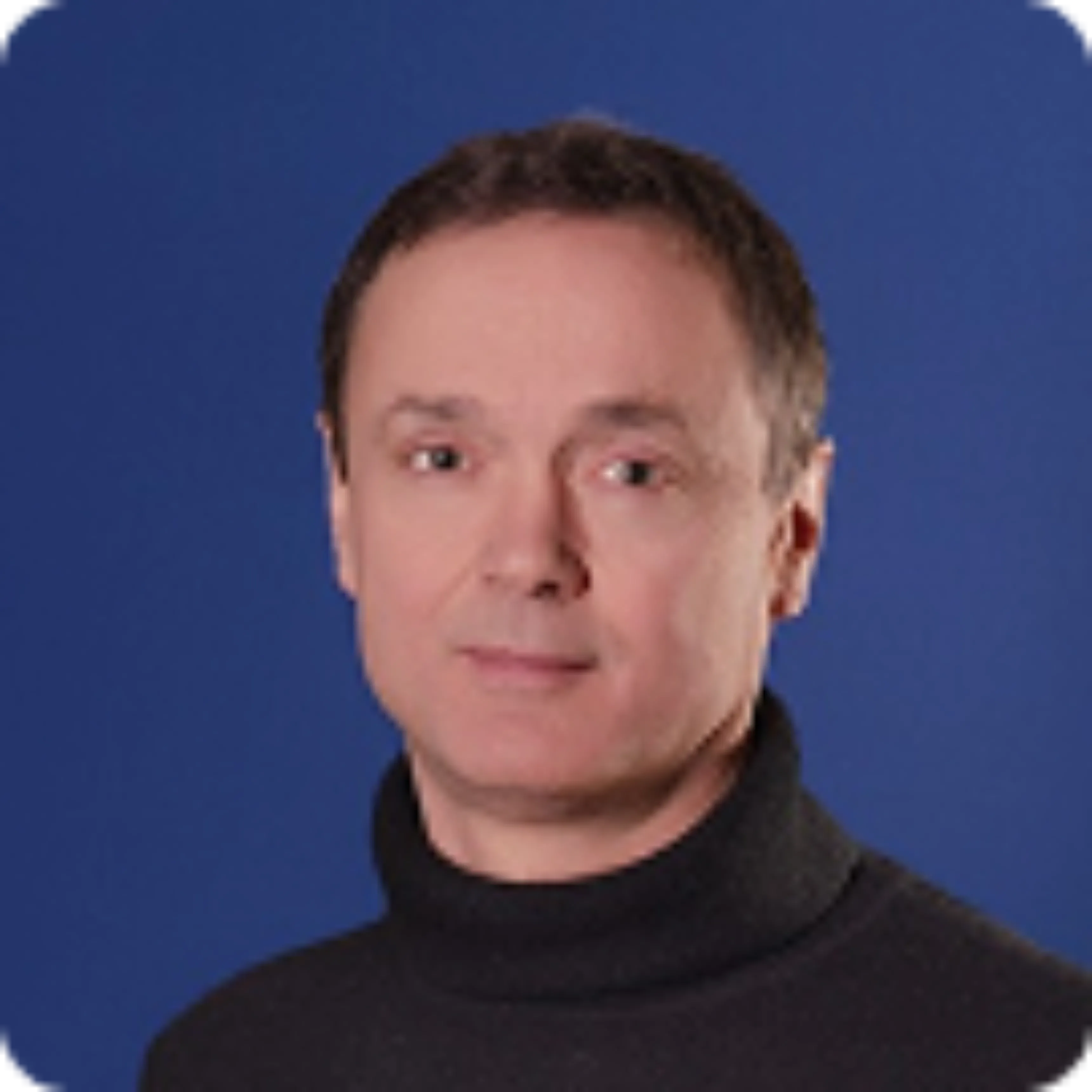 Thomas Saint Hilaire avec un pull noir à col roulé sur un fond bleu uni.