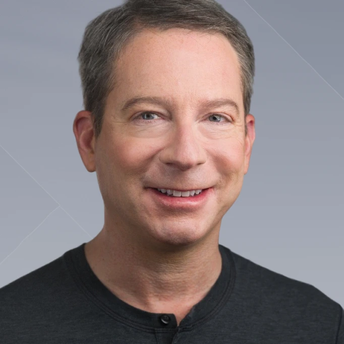 Smiling middle-aged man with short brown hair wearing a dark shirt against a gray background.