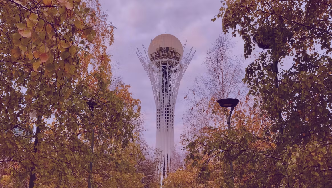 Tower with a golden sphere atop a lattice structure in a park. Autumn trees with golden leaves frame the scene under a purple-tinted sky.