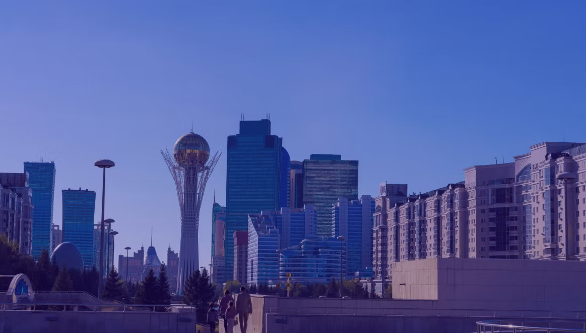 People walk towards modern skyscrapers in a cityscape with a distinctive tower under a blue sky. Urban and calm atmosphere.