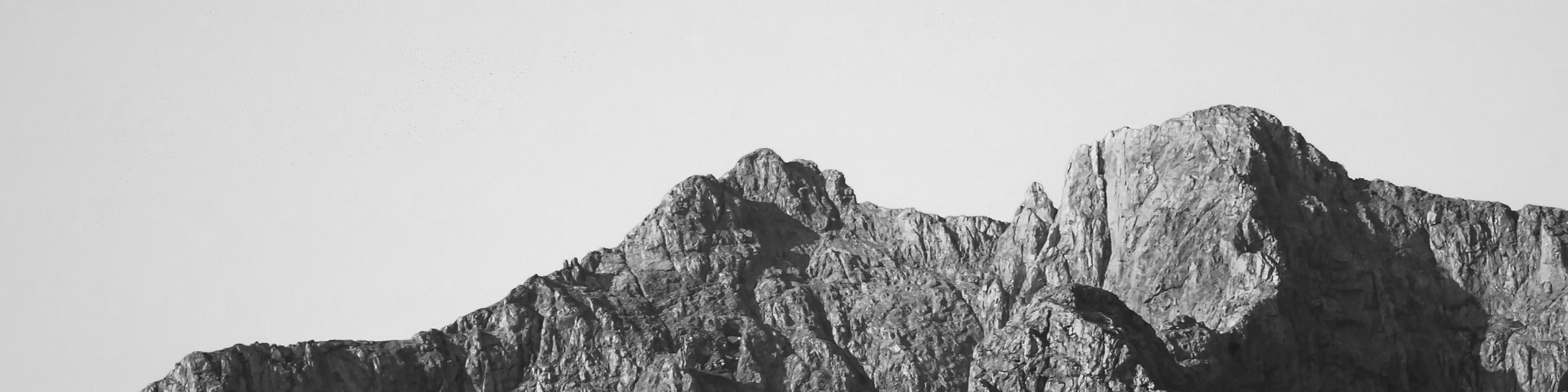 Black and white photograph of a rugged mountain peak under a clear sky.