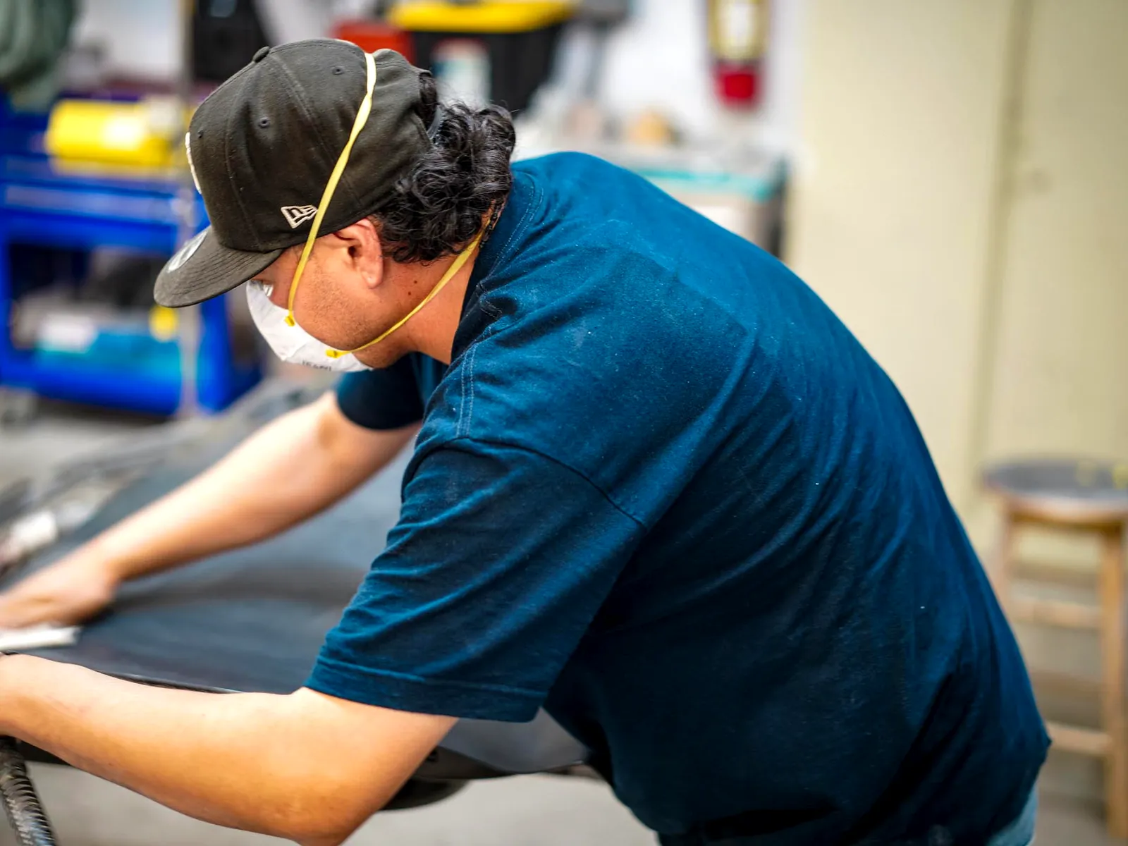 Technician in a respirator preparing a vehicle panel for refinishing
