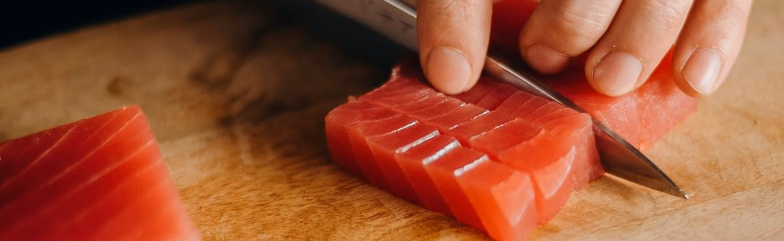 Close-up of hands slicing fresh raw tuna into cubes on a wooden cutting board.
