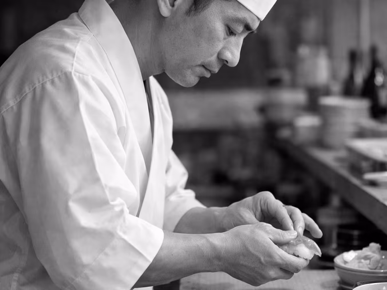 Chef in traditional attire carefully preparing sushi at a counter.