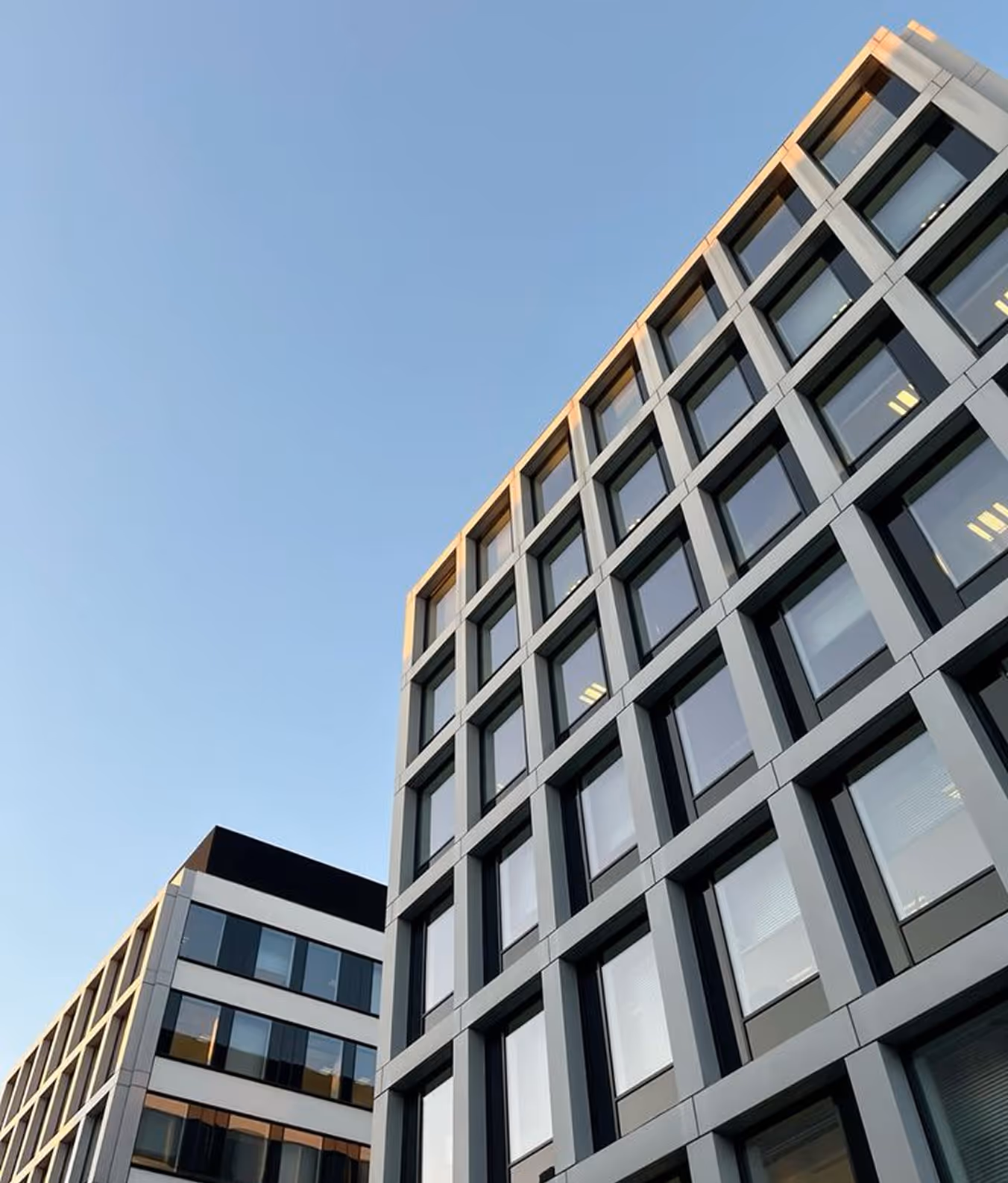 Modern office building with large glass windows under a clear blue sky at sunset.