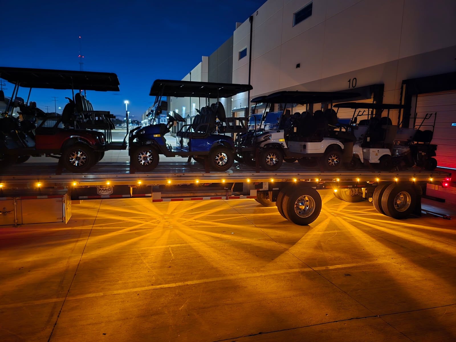 Full truckload of golf carts on a step deck trailer at a distribution center at night