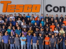 Large group of Tesco employees standing and smiling in front of a building with the Tesco logo.